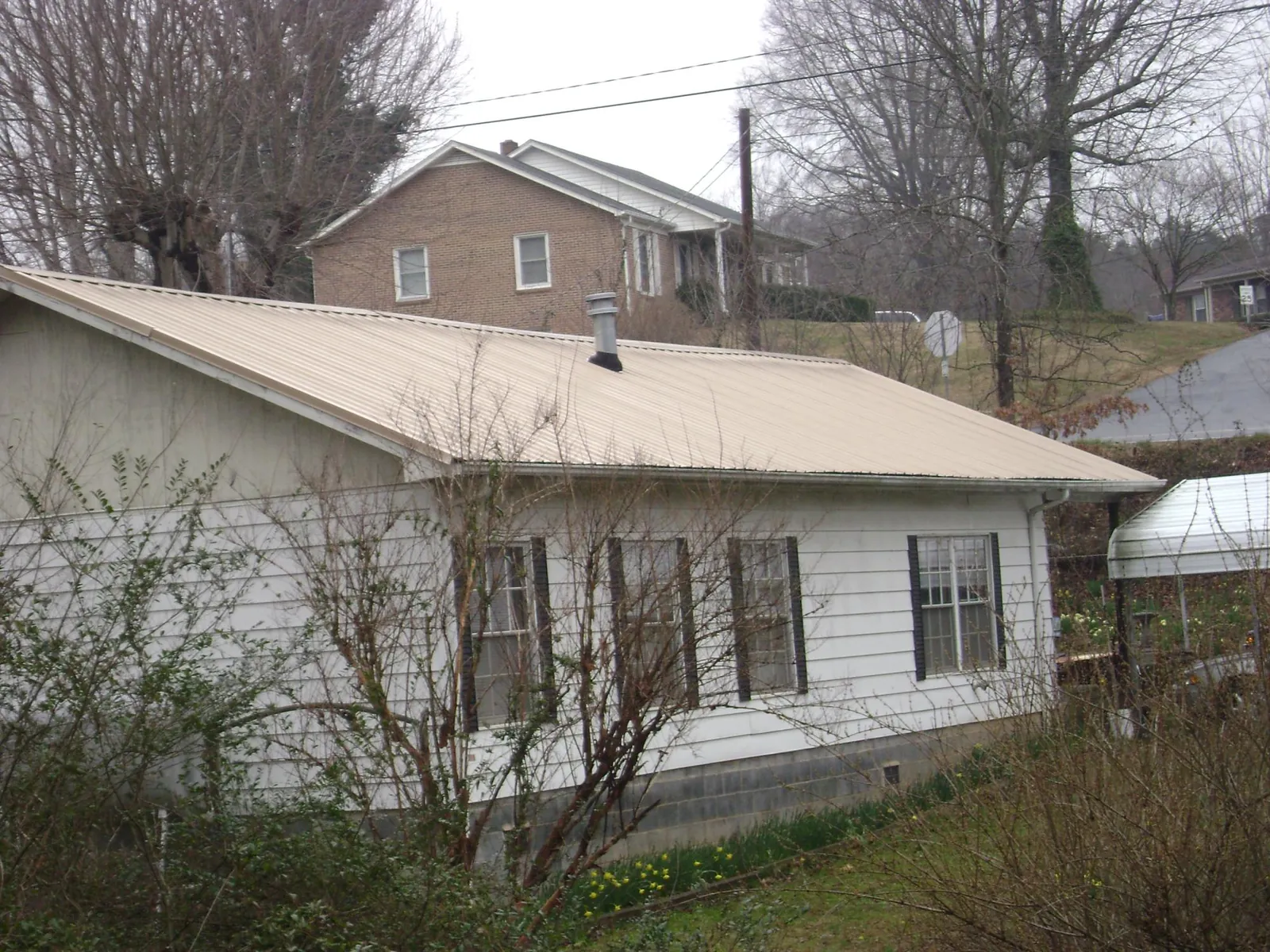 Tan metal roof on a white sided house set into a hillside — Commercial Roofing by Roofing Brothers in Davenport